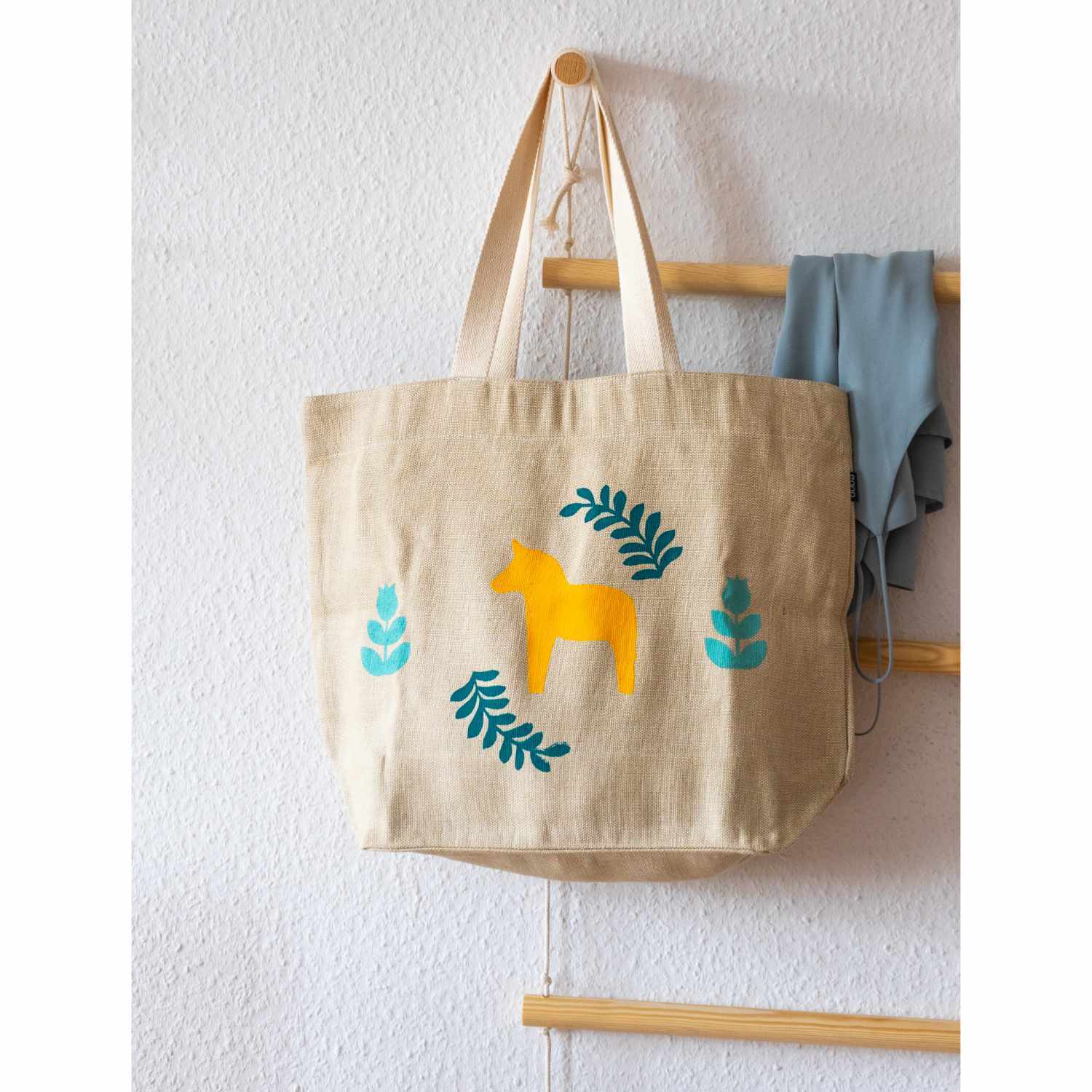 Textil Print Screen Siebdruck Set: Beigefarbene Tasche mit gelbem Pferdemotiv und blauen Blättern, aufgehängt an einer Wand.
