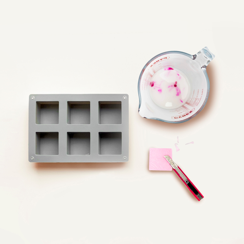 Seifengießform, ein rosa Seifenstück und ein Messbecher mit geschmolzener Seife