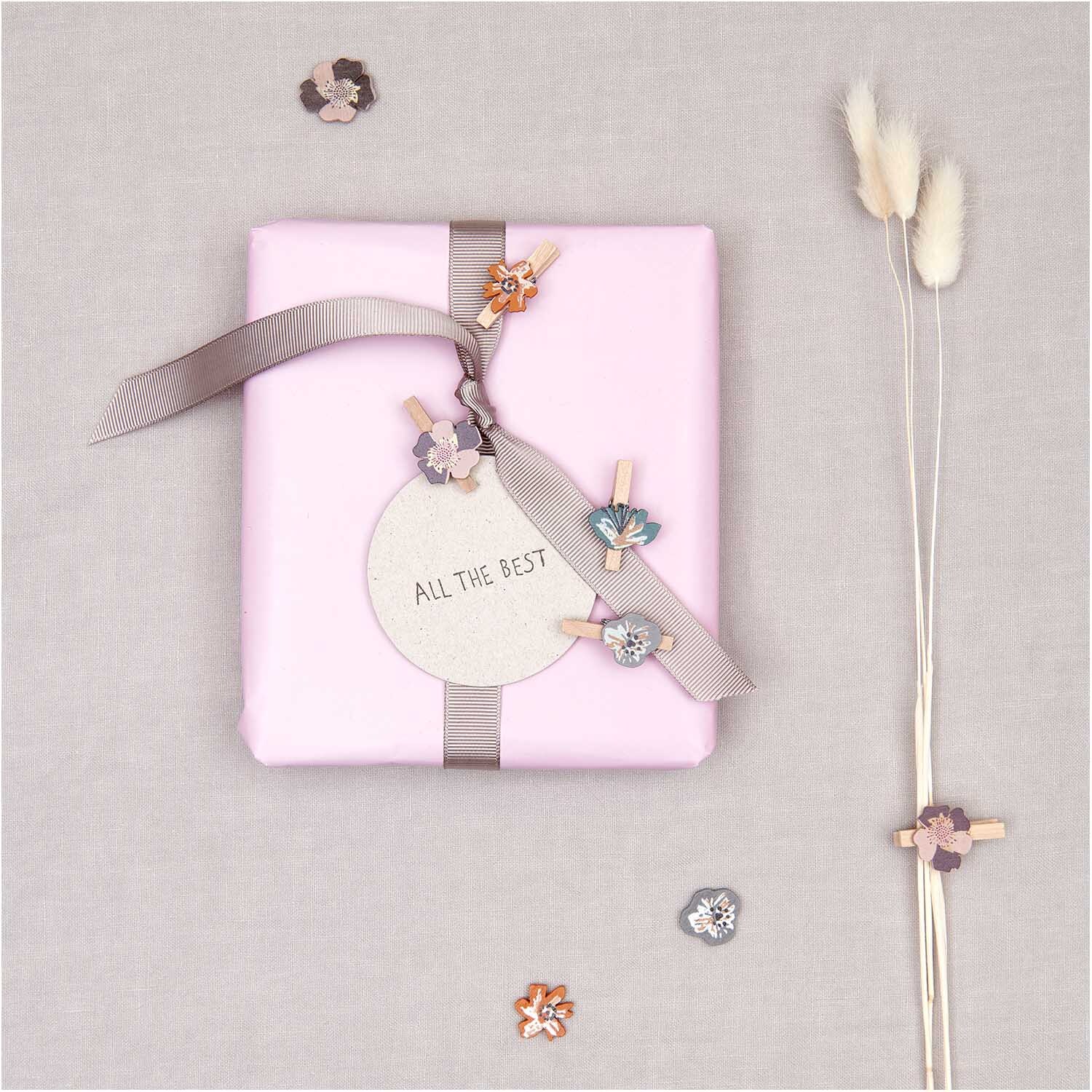 Dekoklammern Blüte 8 Stück von Rico Design auf einem Geschenk mit rosa Papier und Schleife.