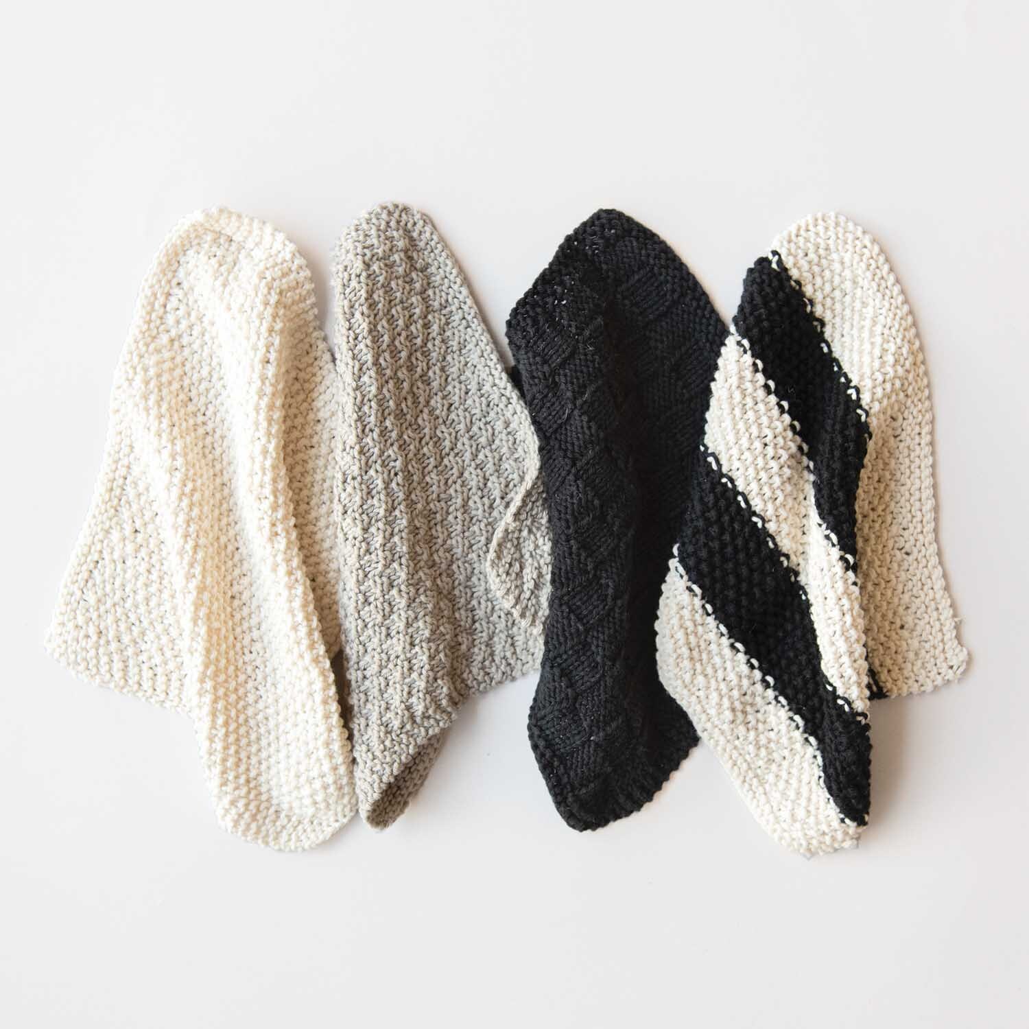 Strickanleitung Spüllappen aus Creative Cotton dk: Vier gestrickte Spüllappen in Creme, Grau und Schwarz auf weißem Hintergrund.