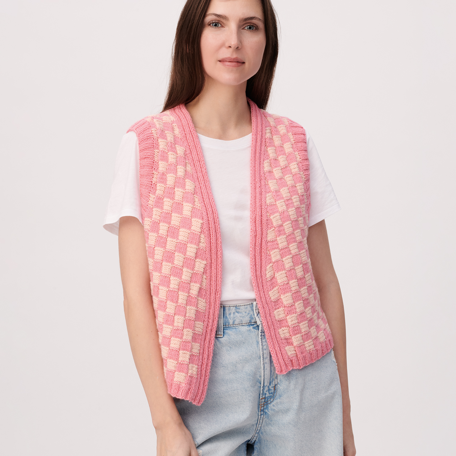 Strickanleitung Damenweste aus Creative Cotton Fleece dk: Frau trägt rosa karierte Weste über weißem T-Shirt und Jeans vor neutralem Hintergrund.