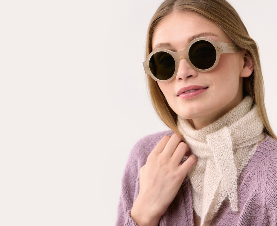 Eine Frau trägt ein Halstuch aus einem hellen Garn gestrickt und eine lila Strickjacke. Modelle aus die Neue Masche No. 9.