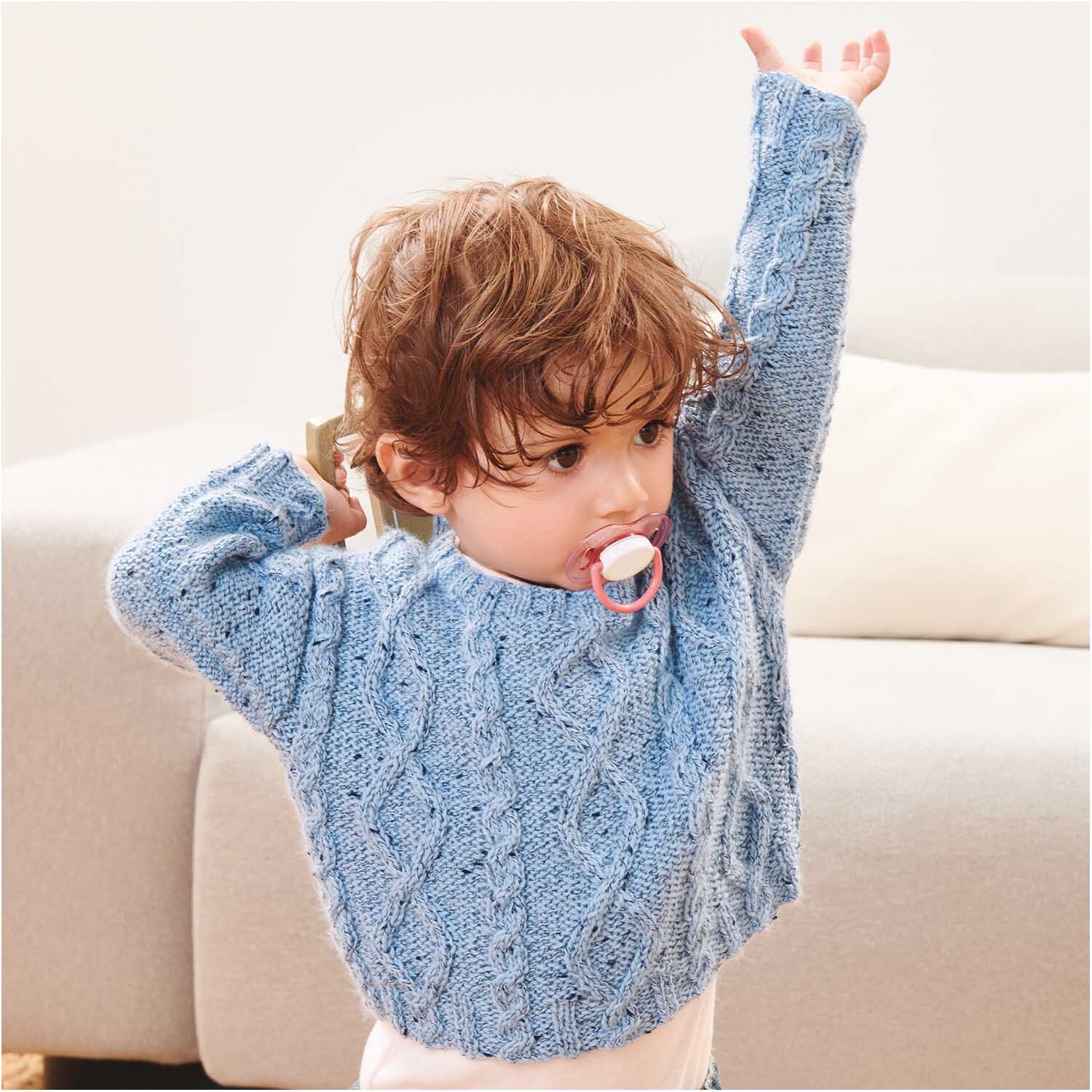 Rico Baby Dream Tweed dk - A Luxury Touch: Ein Kind im blauen Strickpullover hebt die Arme.