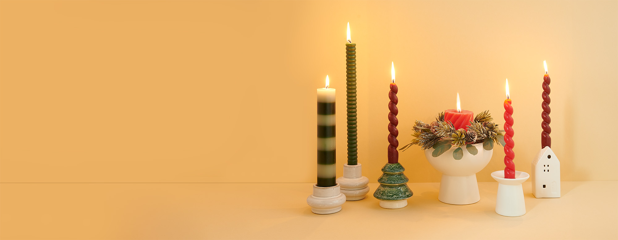 Sechs verschiedene weihnachtliche Kerzenständer mit unterschiedlichen Stab- und Stumpenkerzen. Fotosetting gelber Hintergrund.