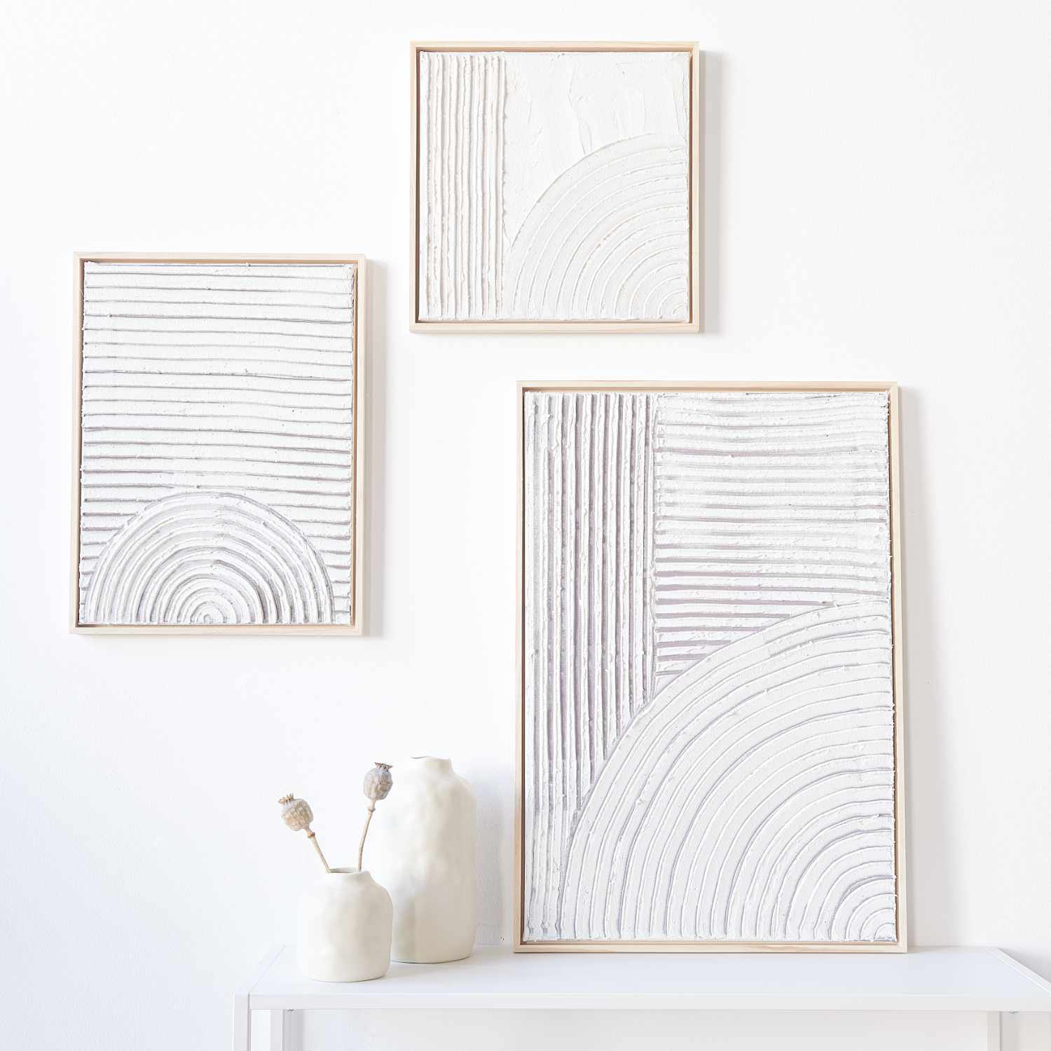 Anleitung Strukturpaste auf Leinwand: Drei minimalistische Leinwände mit weißen, strukturierten Mustern in Holzrahmen an einer weißen Wand.