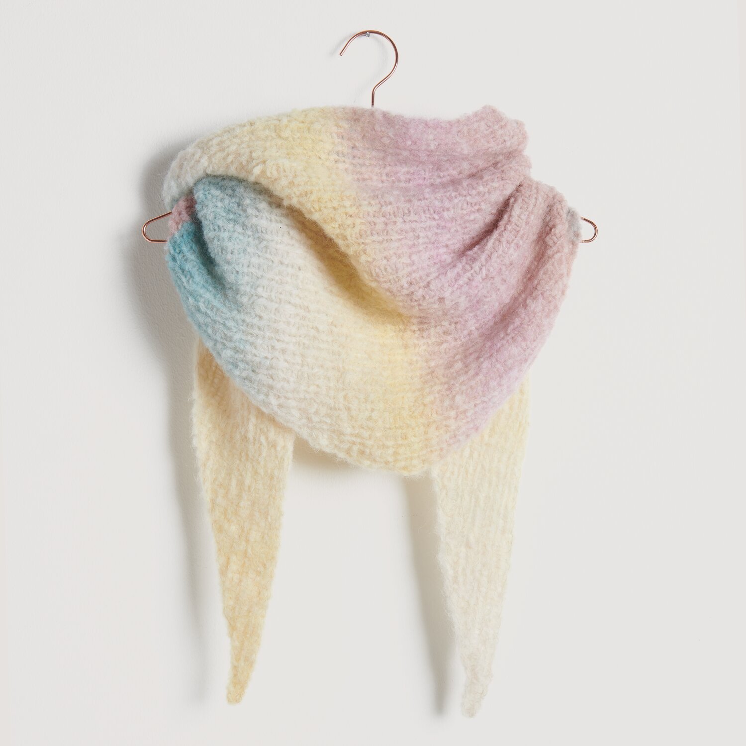 Strickset Dreieckstuch Modell 14 aus Die Neue Masche No. 10 in sanften Pastelltönen auf einem Kleiderbügel.