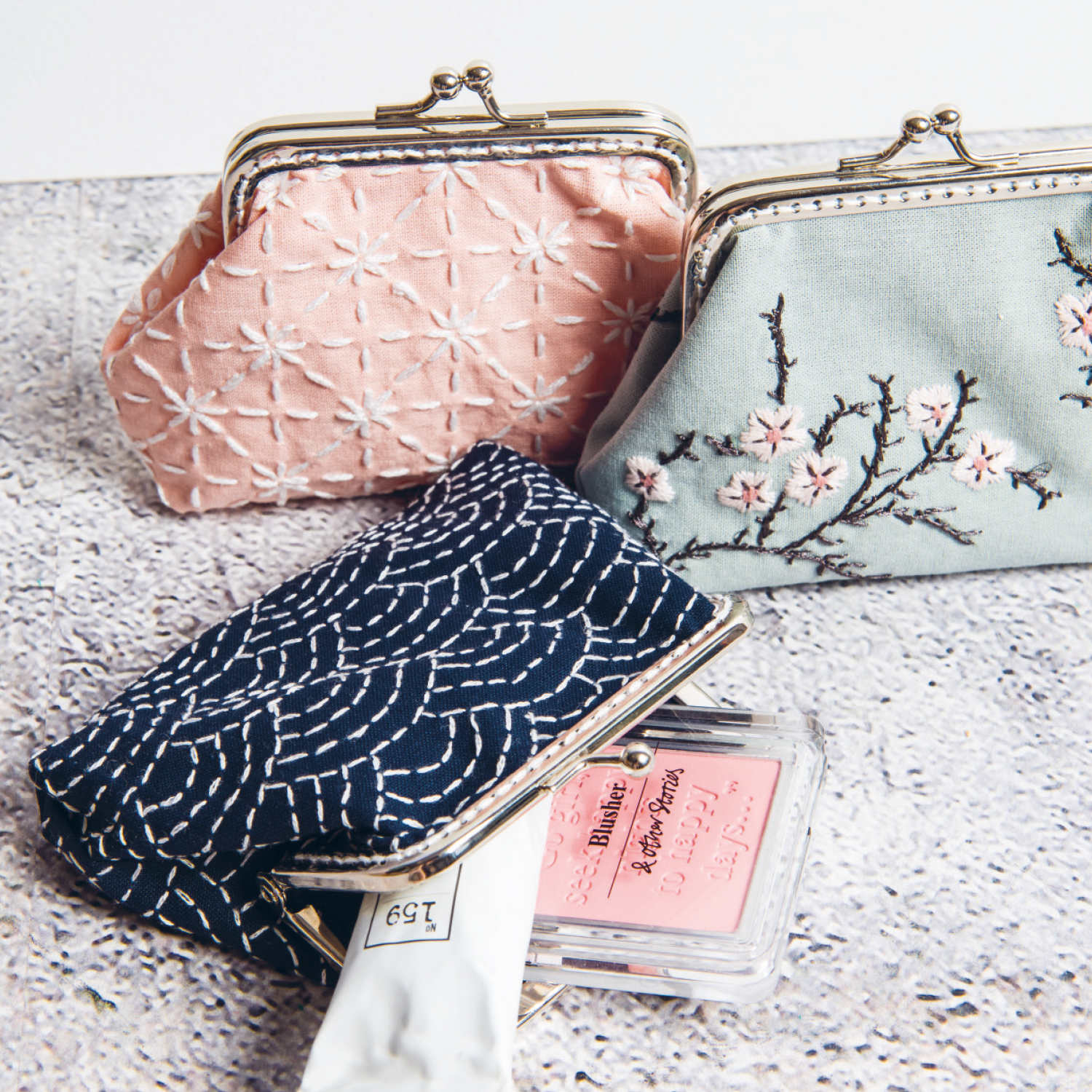 Nähanleitung Sashiko Etui: Drei bestickte Etuis in Pastellfarben mit Sashiko-Muster auf grauem Hintergrund.