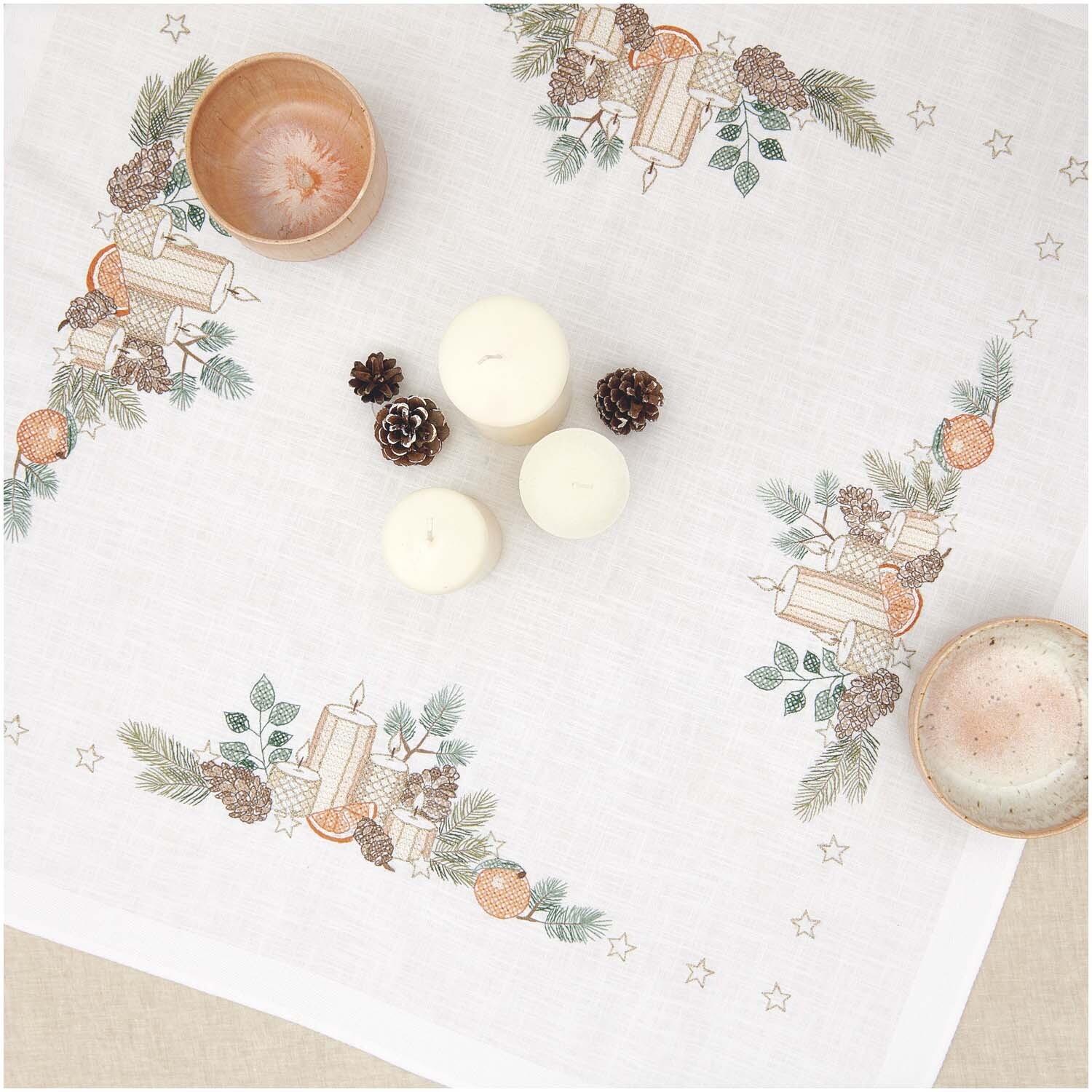 Stickpackung Tischdecke Kerzen 90x90cm mit festlichem Kerzenmotiv und Tannenzweigen, dekoriert mit Zapfen und Orangen auf weißem Hintergrund.