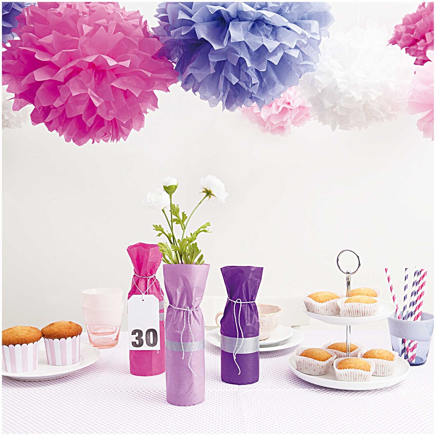 Seidenpapier Pompons in Rosa und Lila von Rico Design schmücken eine festliche Tischdekoration mit Gebäck und Getränken.