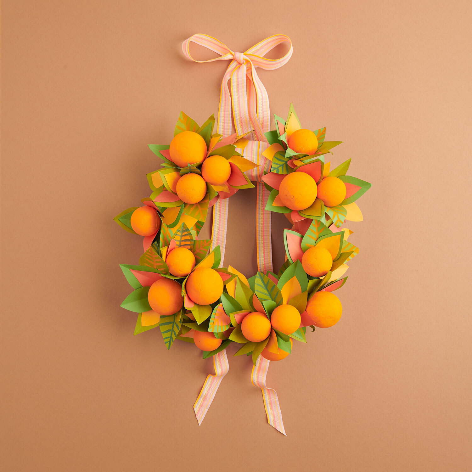 Bastelanleitung herbstlicher Türkranz: Bunter Kranz mit orangefarbenen Kugeln und Blättern auf braunem Hintergrund.