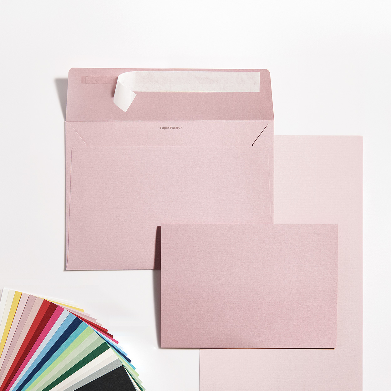 Ein rosa Umschlag mit passender Karte, in der linken Ecke Karten farblich aufgefächert. Flatlay von Produkten aus der Serie Paper Poetry Luxury.