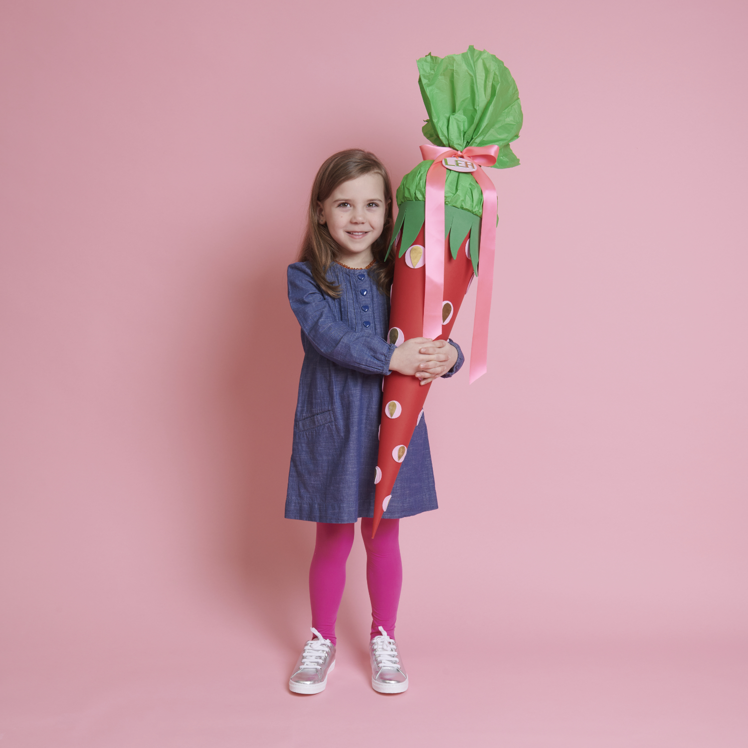 Bastelanleitung Schultüte Erdbeere: Ein Mädchen hält eine rote Schultüte mit grüner Spitze.