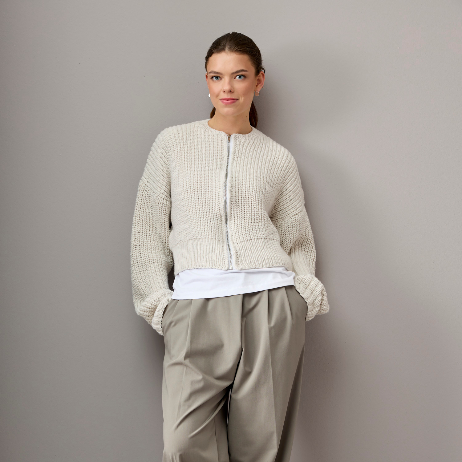 Vegan Cashmere Special: Frau trägt cremefarbene Strickjacke von Rico Design, kombiniert mit weißem Shirt und grauer Hose.