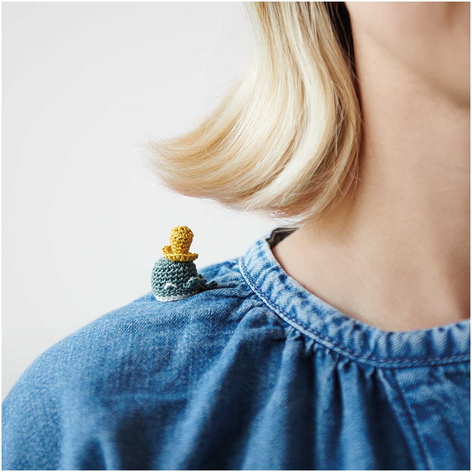 Essentials Crochet: Eine Person trägt ein blaues Oberteil mit einem kleinen, gehäkelten Accessoire auf der Schulter.