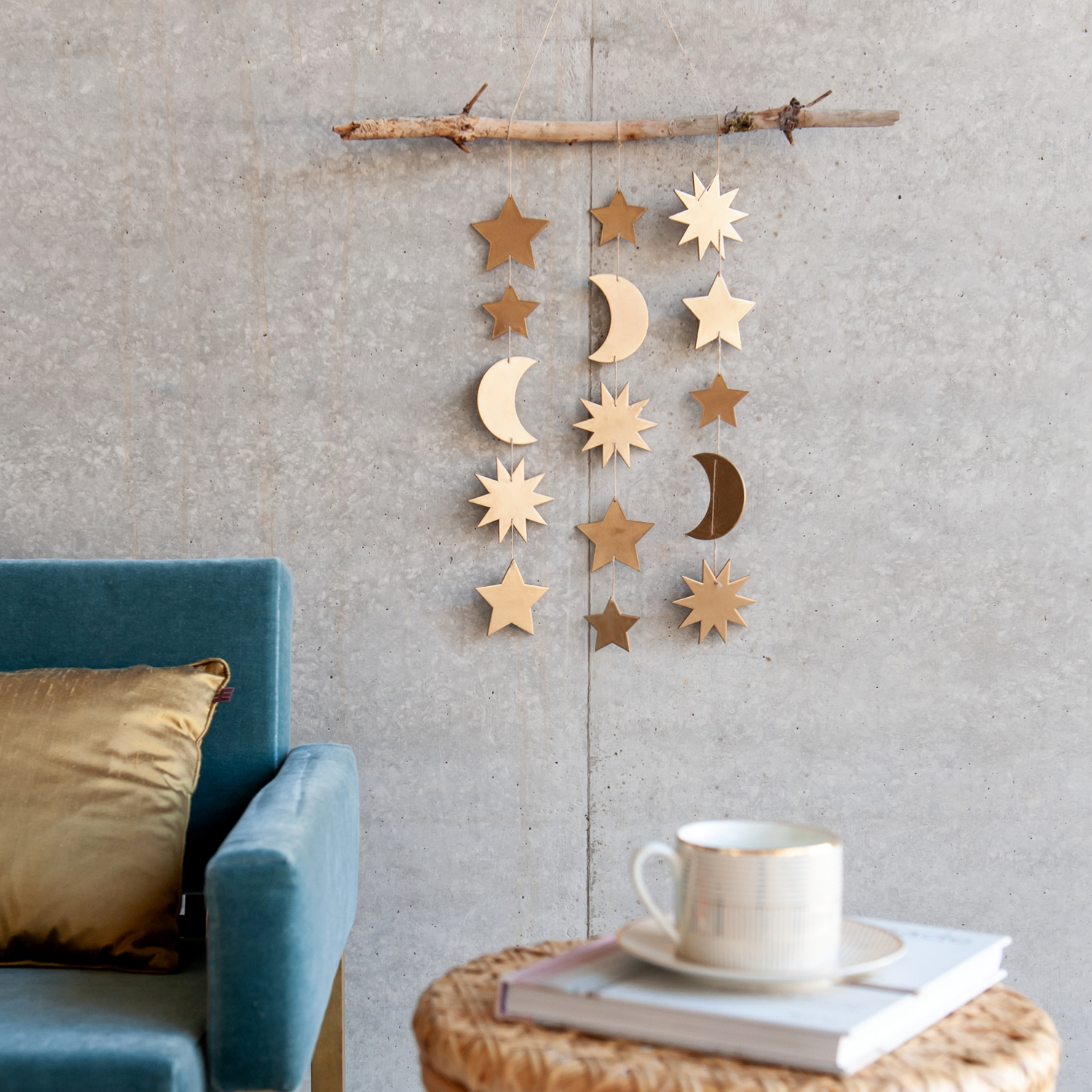 Bastelanleitung Mobilé Sonne und Mond: Hängendes Mobilé aus Holz mit Sternen und Monden an einem Ast, dekorativ vor einer grauen Wand.