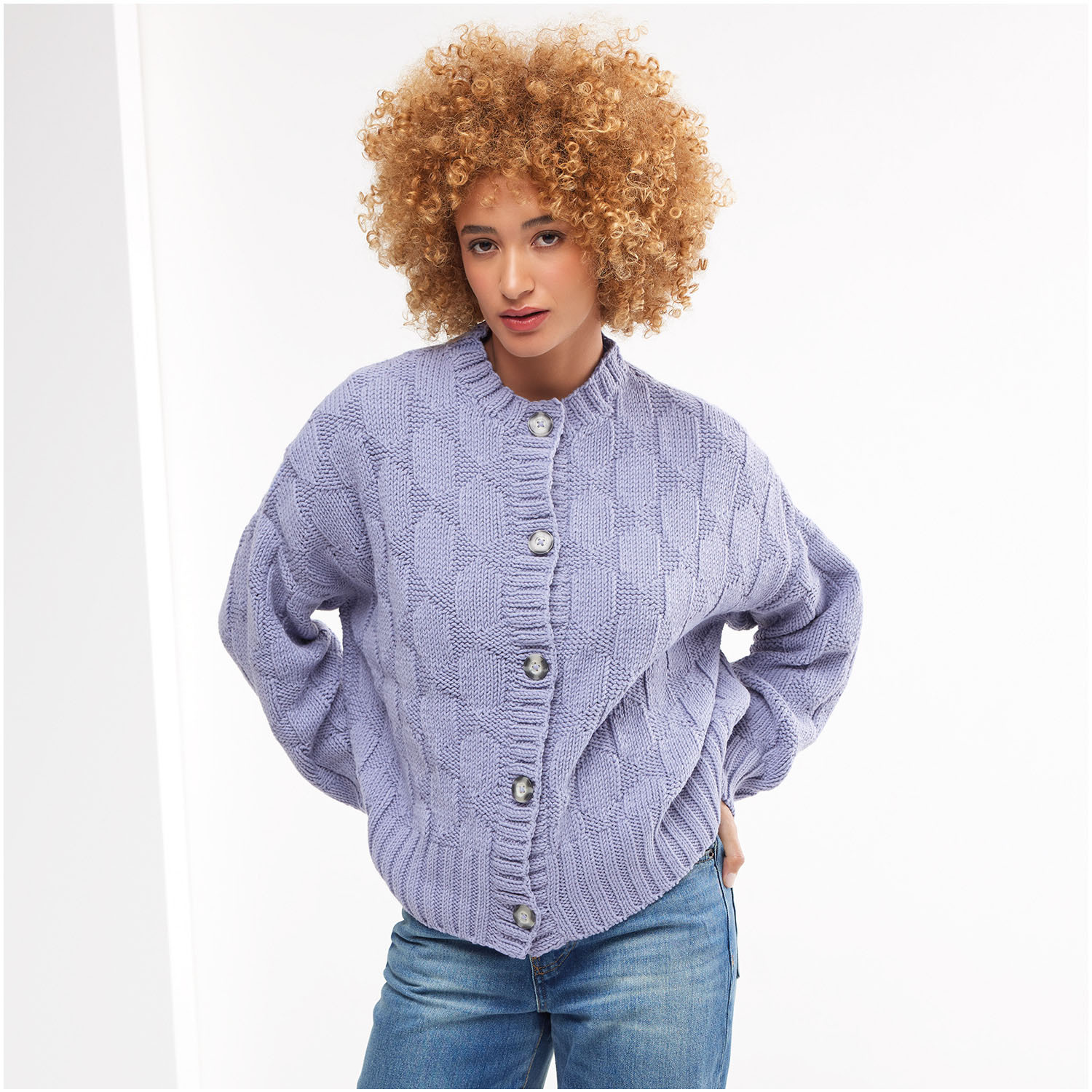 Strickset Jacke Modell 32 aus Die Neue Masche Nr. 8: Lila Strickjacke mit Knopfleiste, getragen von Frau mit lockigem Haar, kombiniert mit blauer Jeans.