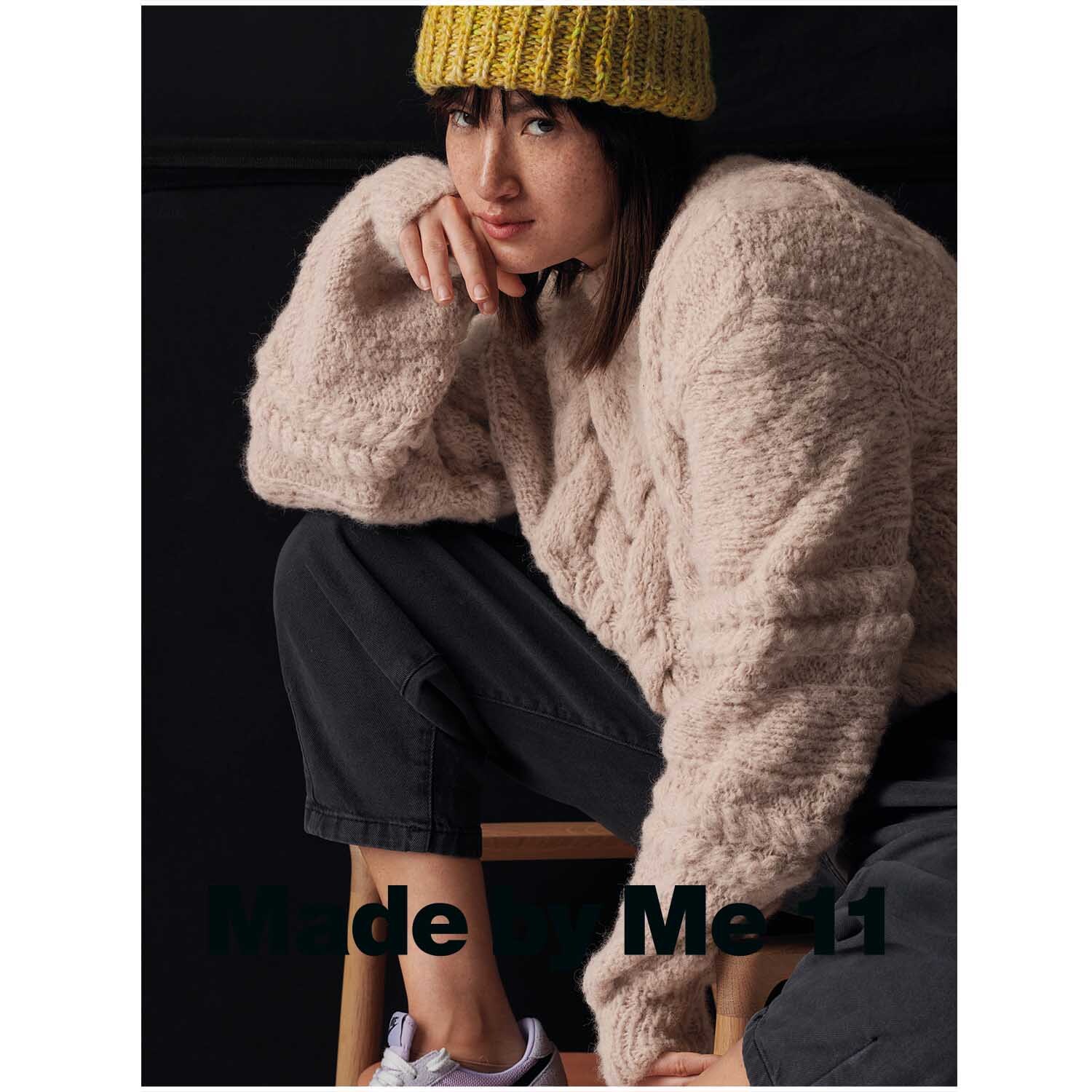 Fashion Light Luxury: Frau in einem beigen Strickpullover und gelber Mütze, sitzt lässig auf einem Stuhl.