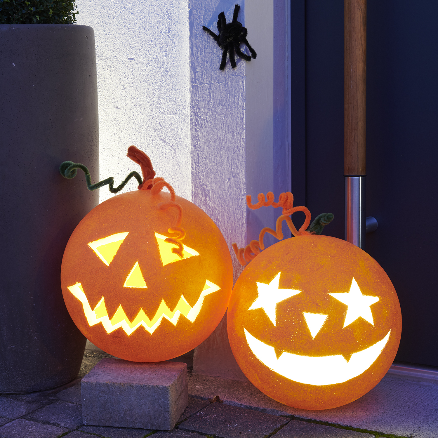 Bastelanleitung Halloweenkürbis aus Polystyrolkugel: Zwei leuchtende Kürbisse mit geschnitzten Gesichtern vor einer Haustür.