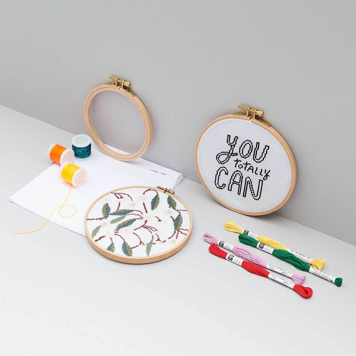 Zwei bestickte Stickringe mit unterschiedlichem Stickgarn und leerem Stickring. Fotosetting graue Ecke.