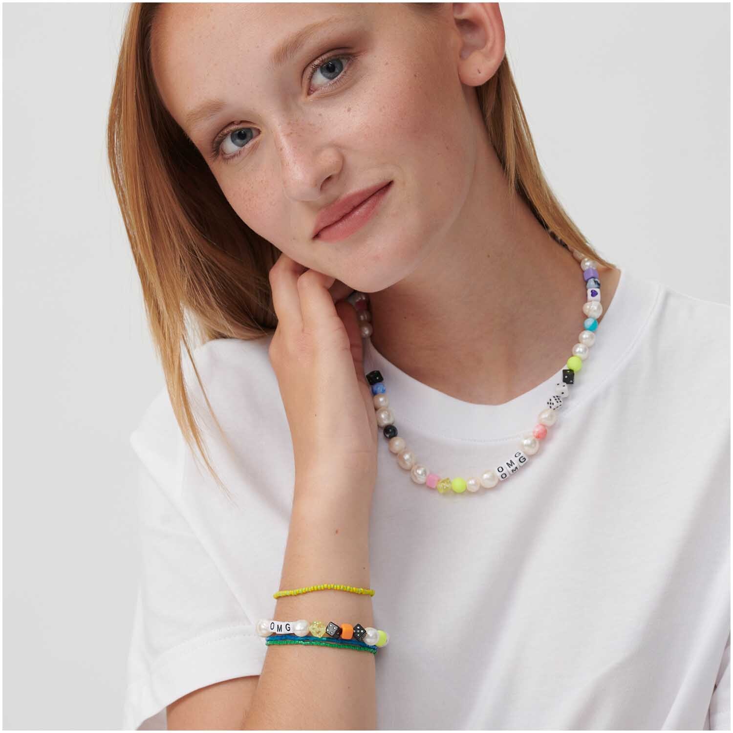 Itoshii Perlen Würfel 6mm 96 Stück von Rico Design, getragen als bunter Schmuck auf weißem T-Shirt.