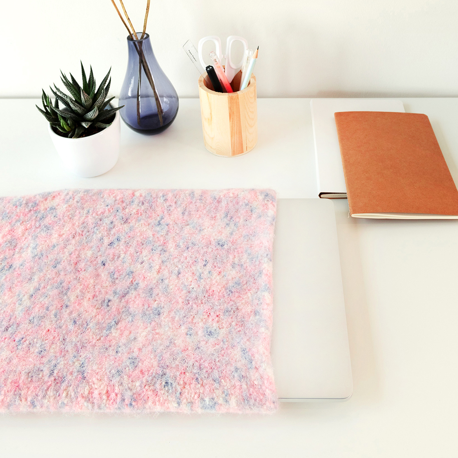 Strick-\/ Häkelanleitung Filz-Laptoptasche: Rosa Filztasche auf einem Schreibtisch mit Pflanzen und Schreibutensilien.