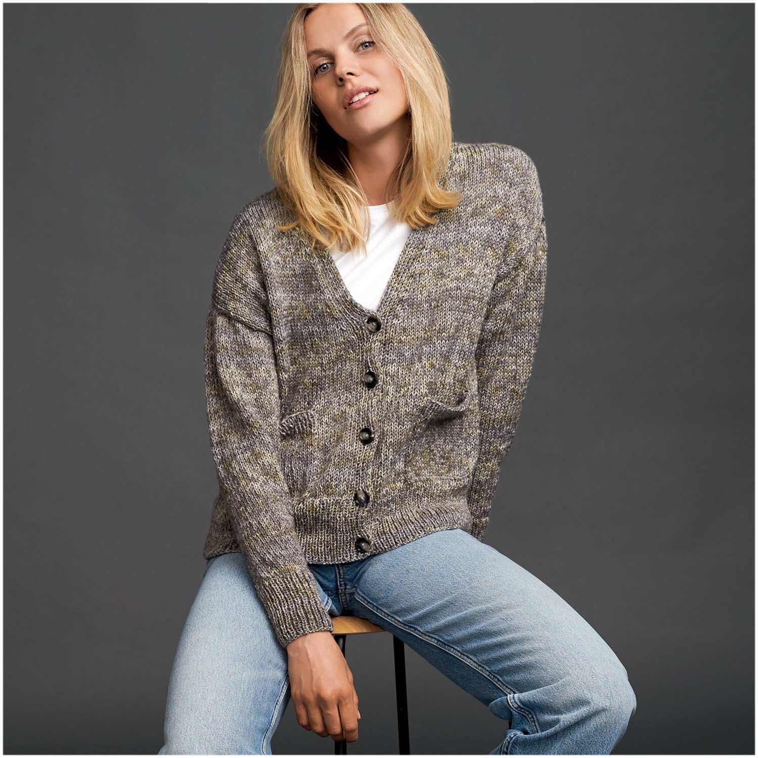 Superba Easy 8 8fädig Strickjacke in melierter Optik, getragen von einer Frau auf einem Hocker.