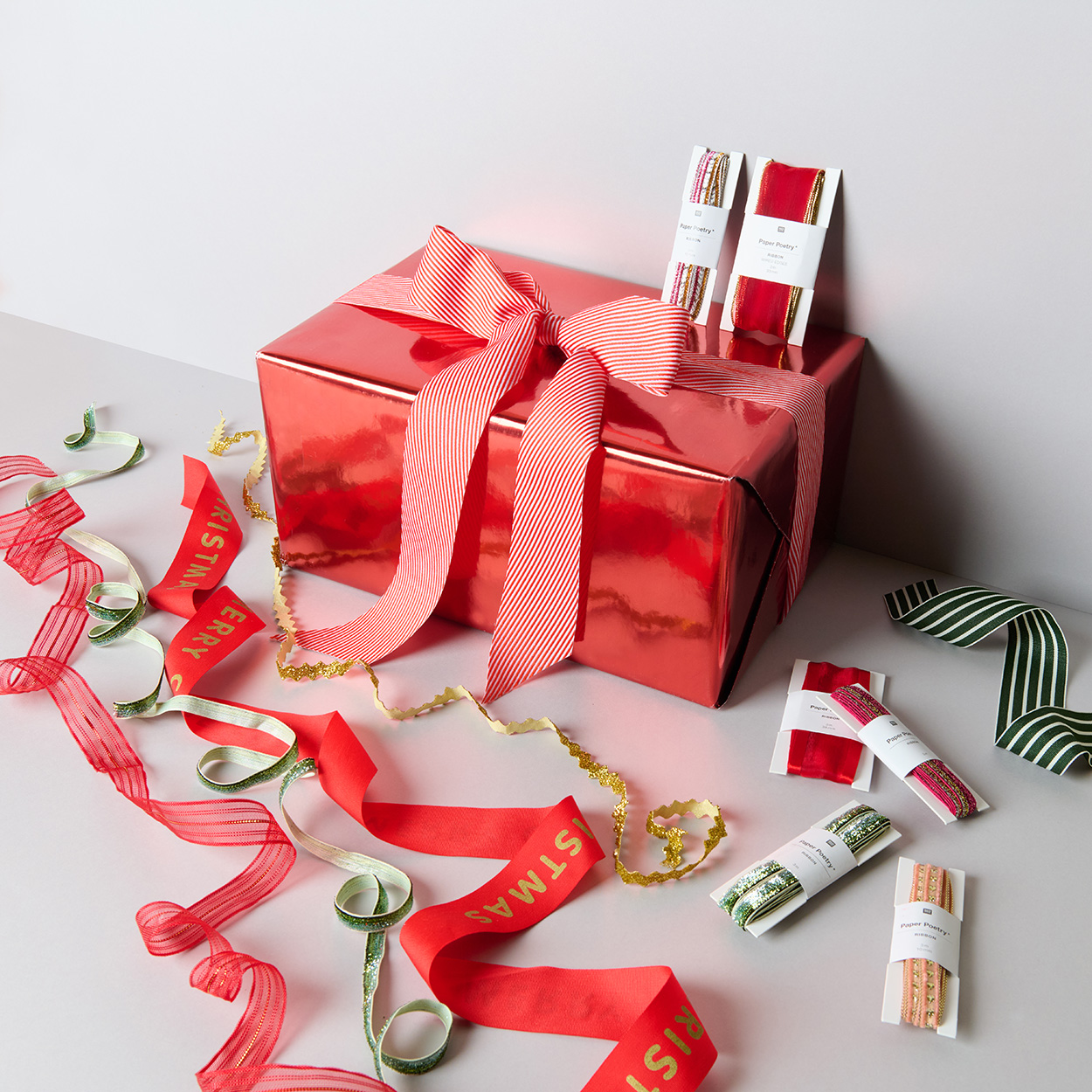 Weihnachtliches Geschenkband ausgerollt und in der Verpackung mit rot verpacktem Geschenk. Fotosetting graue Ecke.