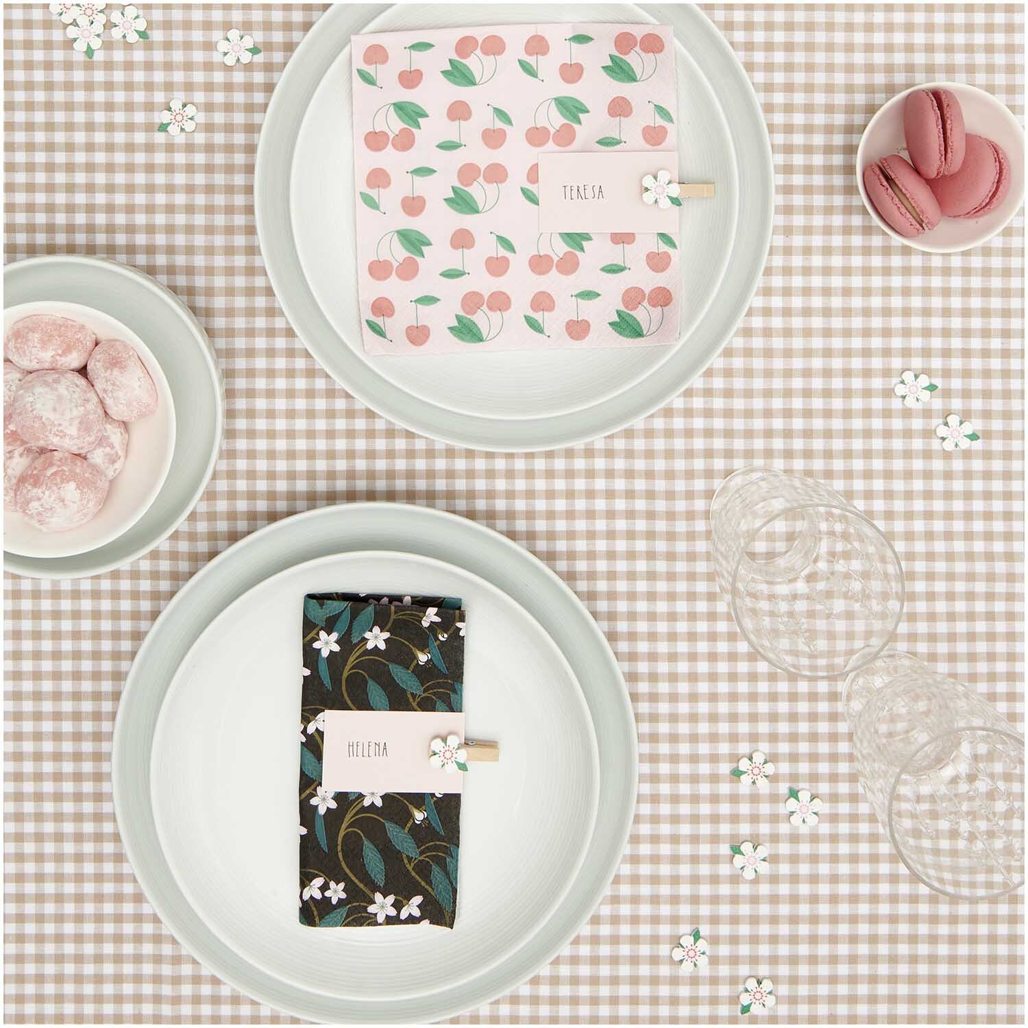 Servietten Kirschblütenranken 33x33cm von Rico Design auf einem karierten Tisch mit Geschirr und rosa Macarons.