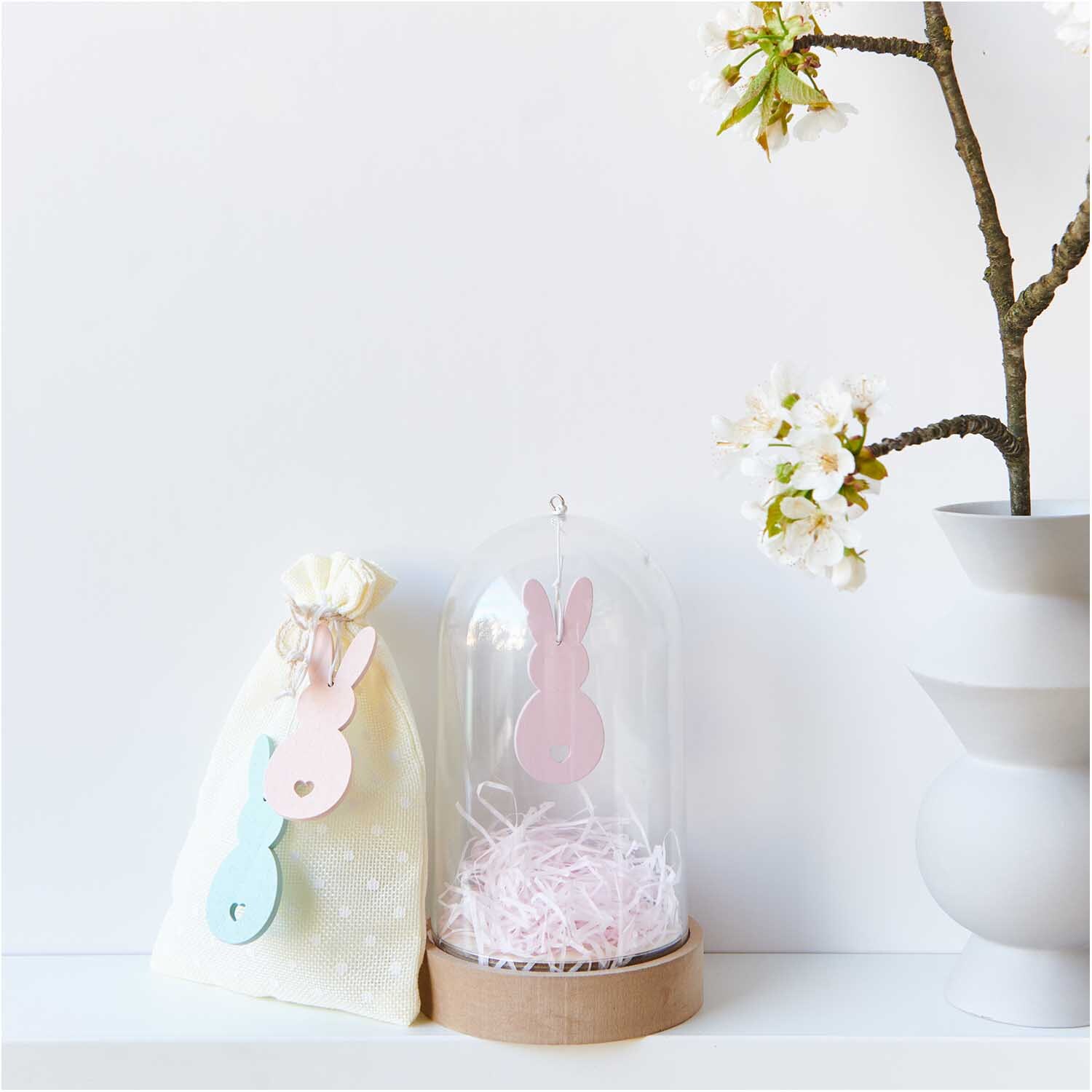 Holzhänger Hase 2 Stück von Rico Design: Zwei dekorative Hasenanhänger in Pastellfarben neben einer Vase mit blühendem Zweig.