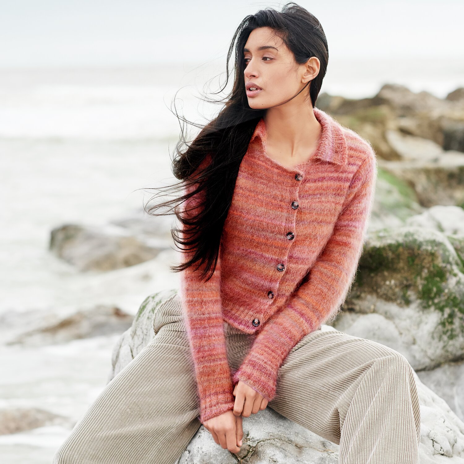 Strickset Jacke Modell 40: Frau trägt eine rotbraune Strickjacke am Strand, kombiniert mit beigen Cordhosen.