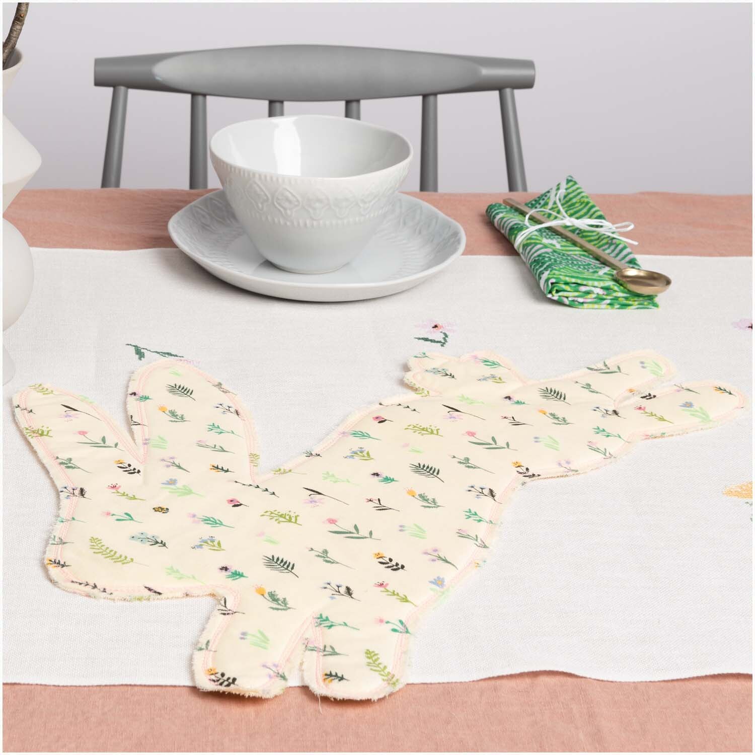 Musselin-Druckstoff Bunny Hop Streublumen auf Tisch mit Geschirr und Besteck, ideal für kreative Nähprojekte.