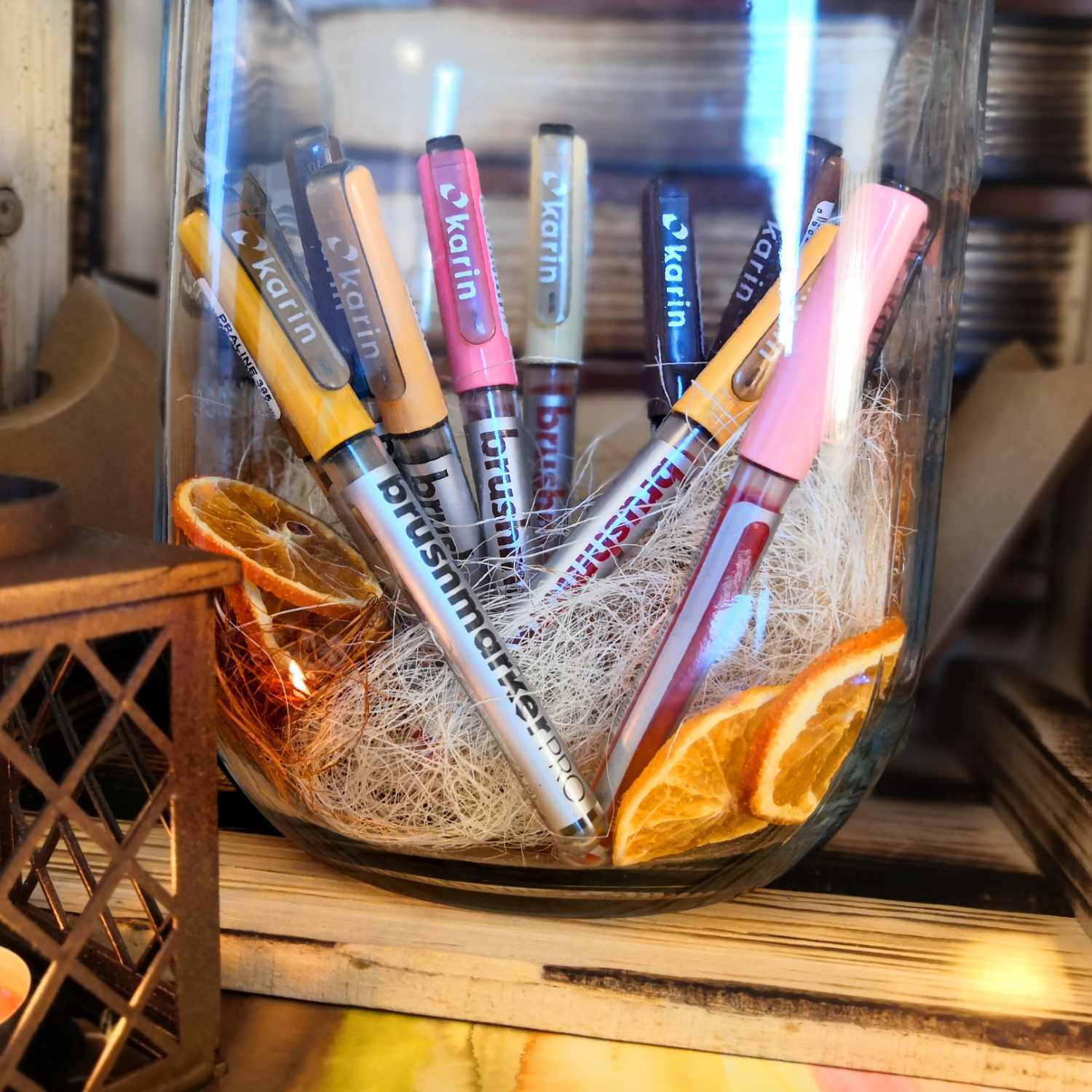 Brushmarker PRO in einem Glas mit getrockneten Orangenscheiben, umgeben von dekorativen Elementen. Markenname: karin.