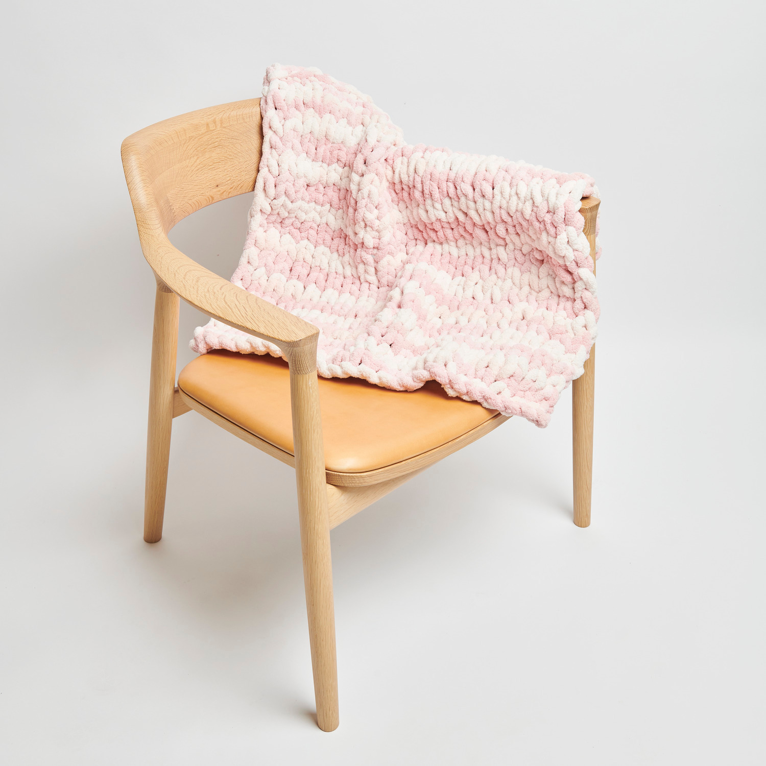 Chenillove Super Big Print: Weiche rosa Decke von Rico Design auf einem modernen Holzstuhl drapiert.