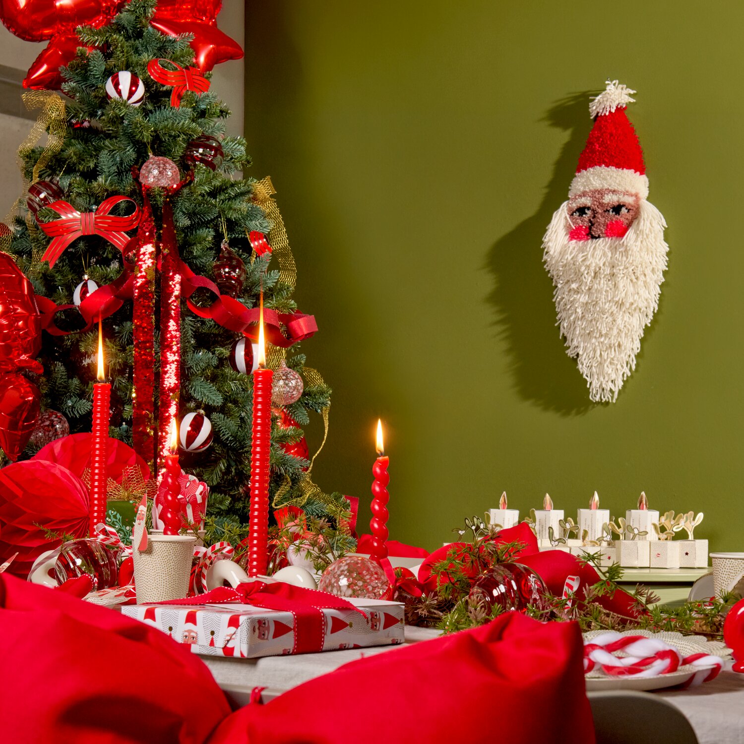Punch Needle Packung Kissen Santa, festliche rote Weihnachtsdeko mit Kerzen, Baumschmuck, Geschenkbändern und Wand-Santa vor grüner Wand