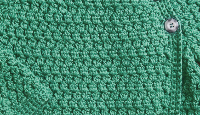 Häkelanleitung Jacke aus Baby Dream dk Uni: Nahaufnahme einer grünen, gehäkelten Jacke mit Knopfdetail.