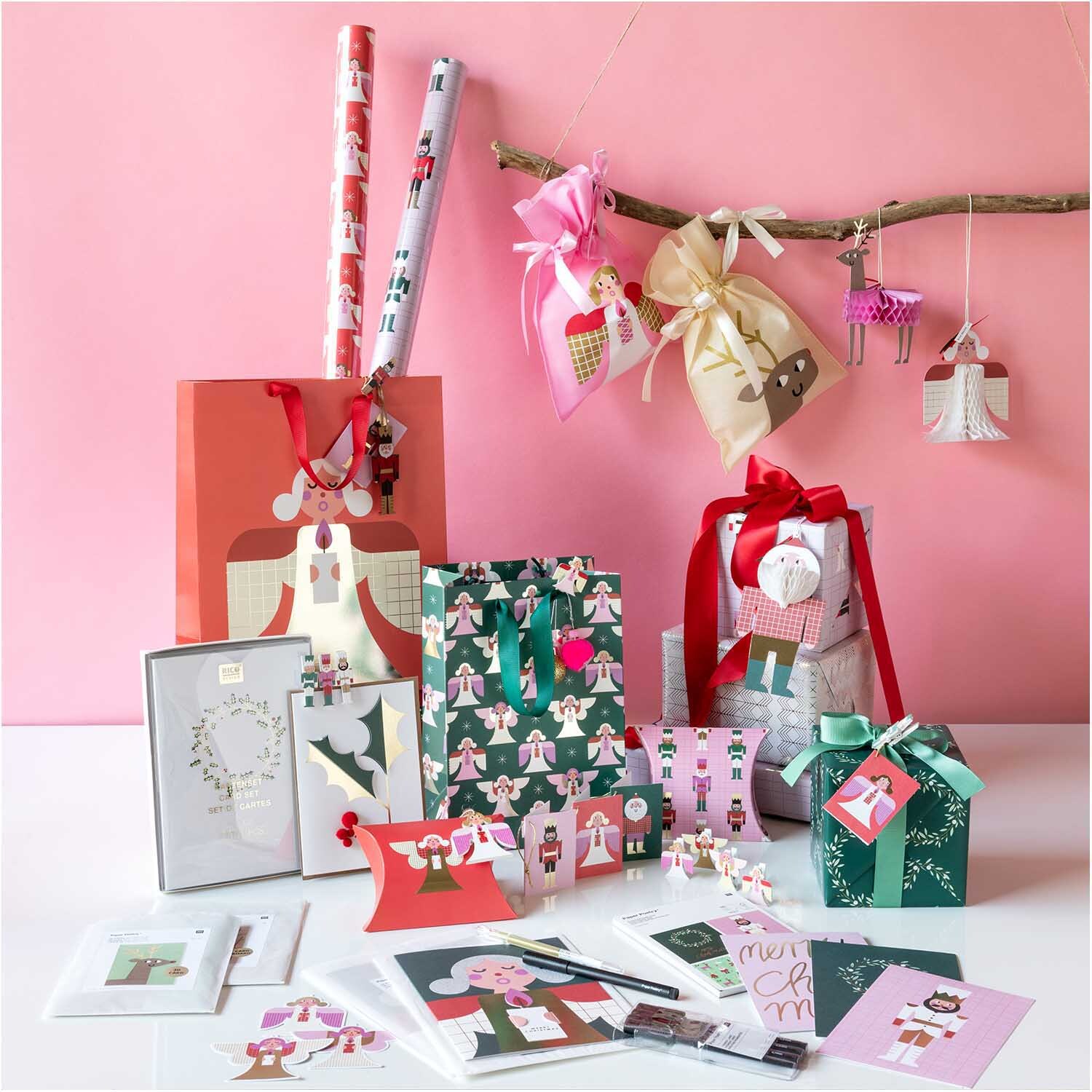 Paper Poetry Geschenkschachtel Weihnachtsfiguren 4 Stück, dekorativ arrangiert mit bunten Geschenkverpackungen und Karten vor rosa Hintergrund.
