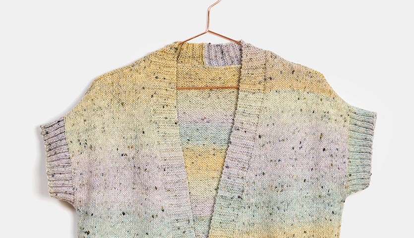 Strickanleitung Weste aus Fashion Cotton Light & Long Tweed dk, gestrickt in sanften Pastelltönen, auf einem Kleiderbügel präsentiert.