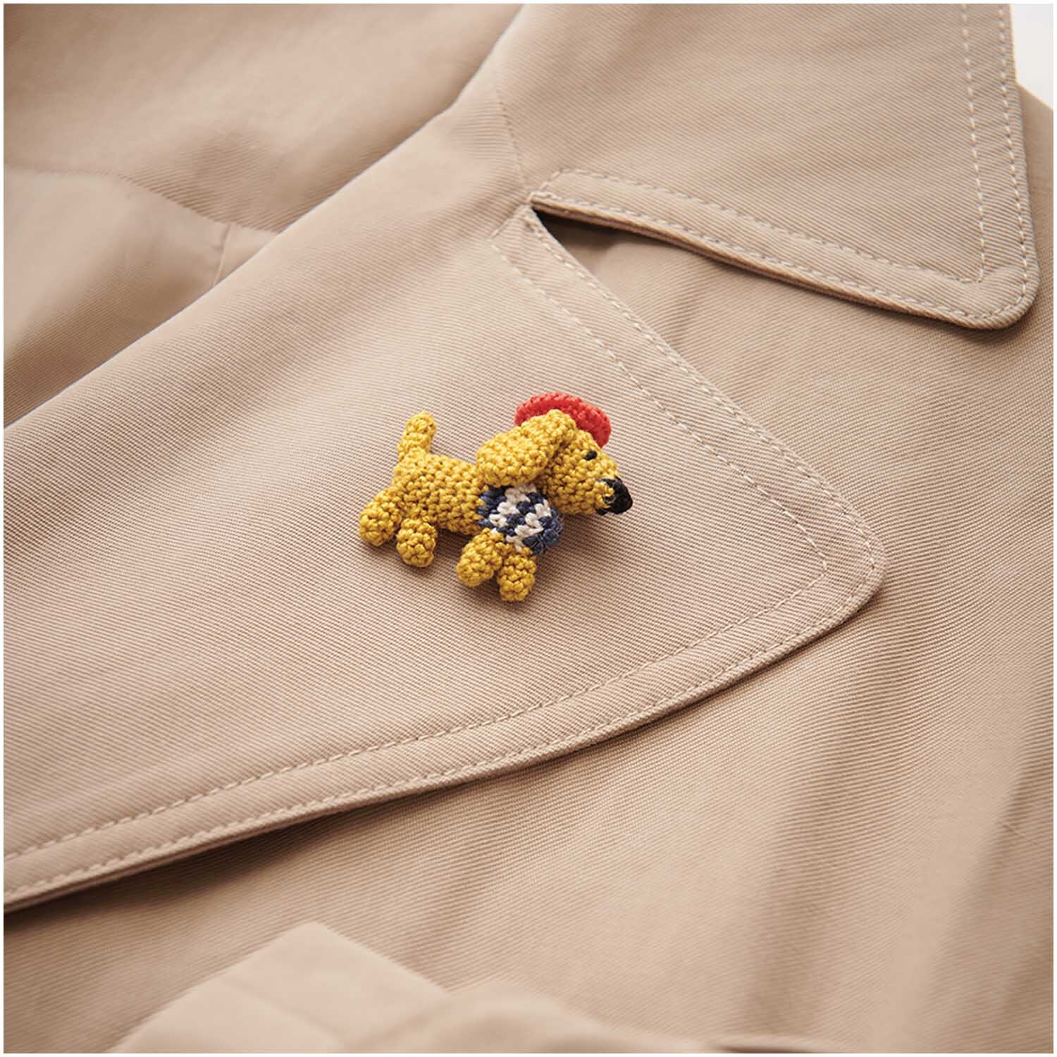 Essentials Crochet: Ein cremefarbener Mantel mit einem gehäkelten Hundebrosche von Rico Design.