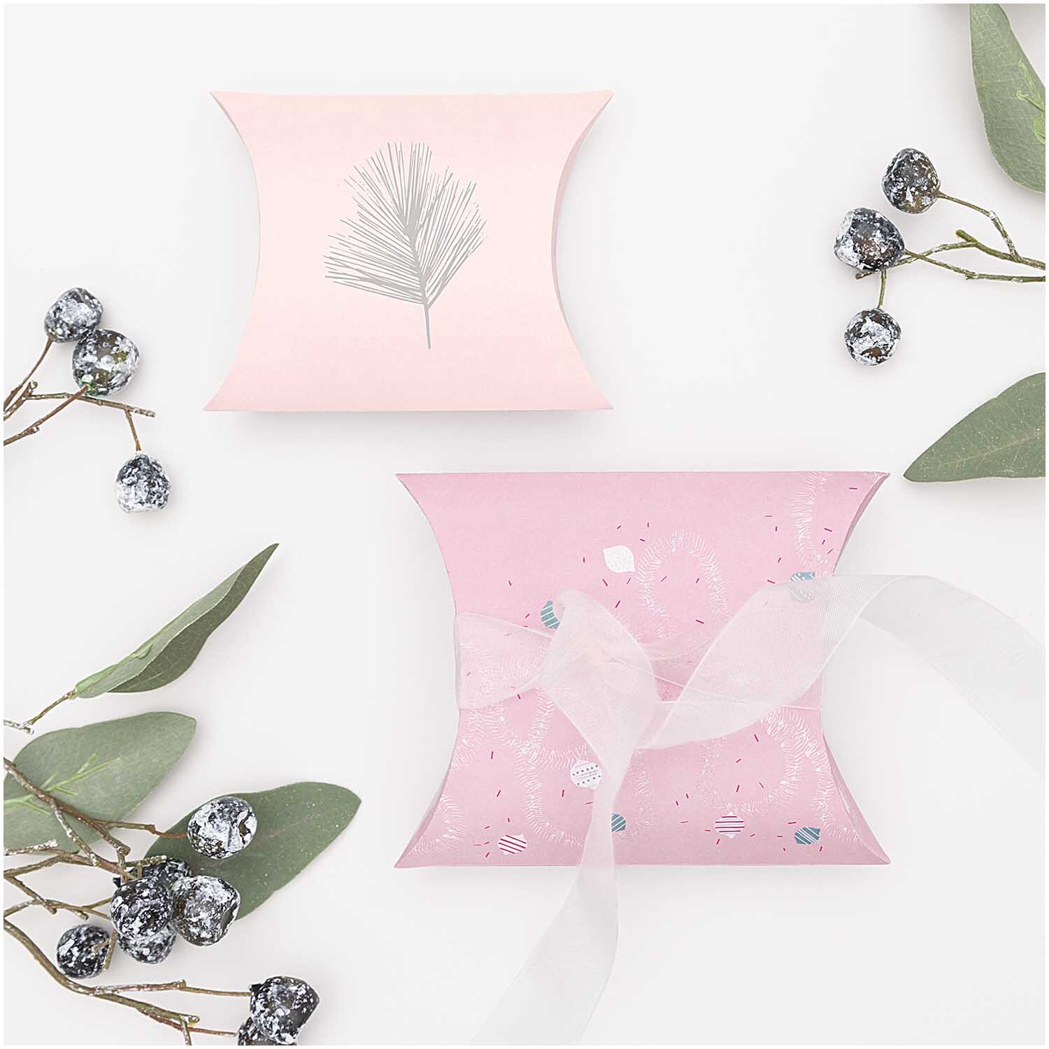 Paper Poetry Geschenkschachteln zeigen zwei rosa Schachteln mit weihnachtlichen Motiven, umgeben von Zweigen und Beeren.