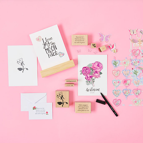 Vier weiße Karten mit Blumen und Sprüchen verziert, dazu verschiedene Stempel und Glanzbilder. Produkte aus der Kollektion La Vie En Rose.