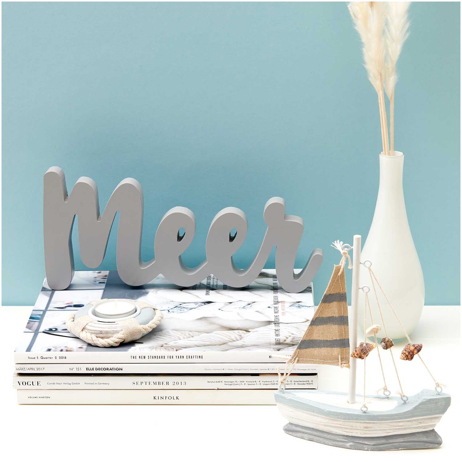 Segelboot aus Holz 15x18cm vor einem blauen Hintergrund, dekoriert mit einem Schriftzug "Meer" und einer Vase.