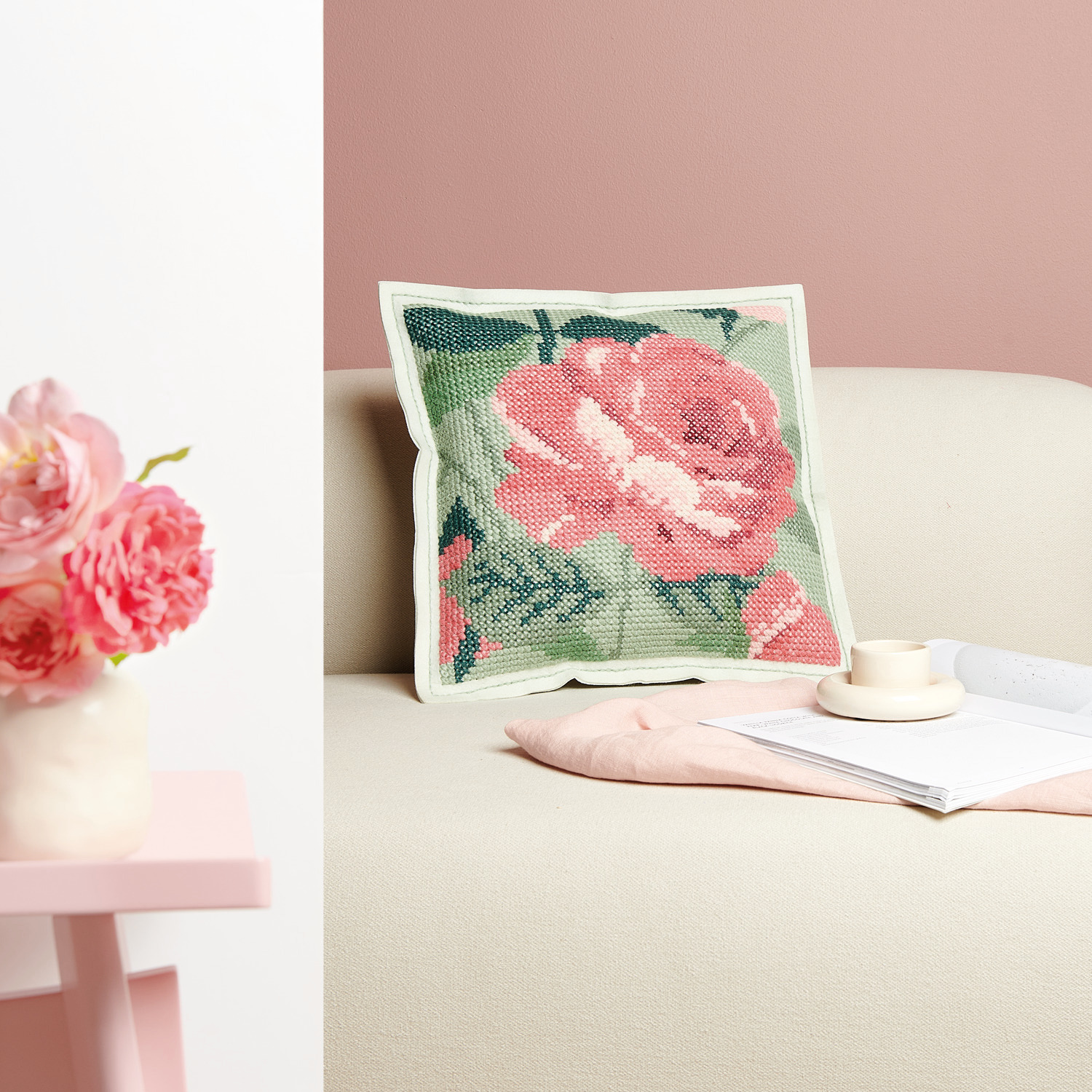 Filzkissen zum Besticken Rose, 42x42cm, zeigt ein florales Design in Rosa und Grün auf einem Sofa.