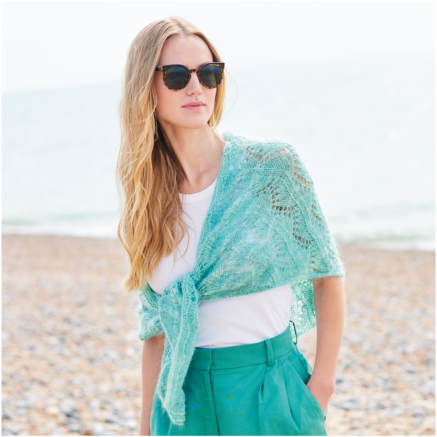 Strickset Dreieckstuch Modell 23: Frau am Strand mit türkisfarbenem Tuch und Sonnenbrille.
