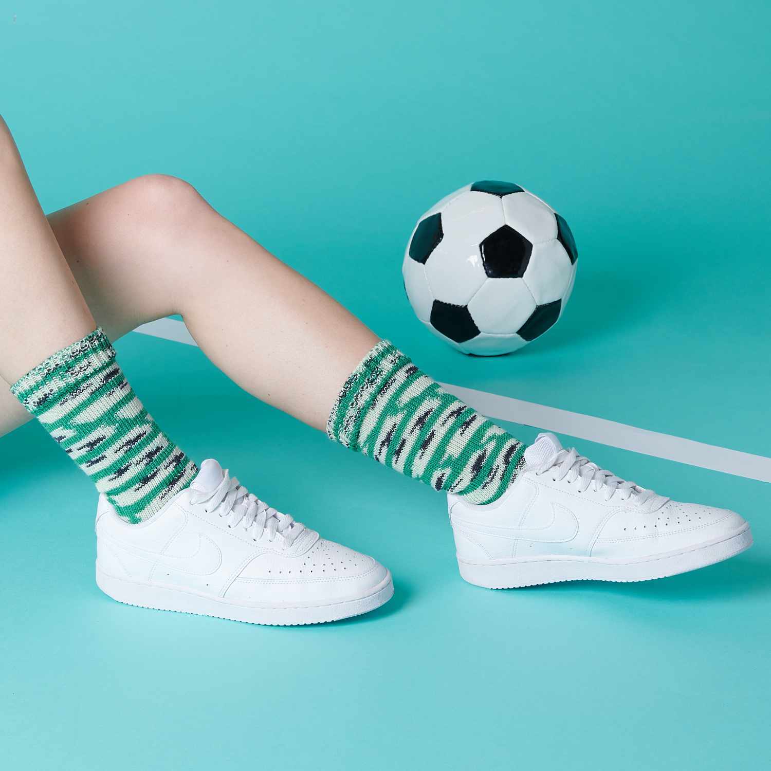Superba Footballs 4fädig: Person mit grünen Socken und weißen Sneakers vor einem Fußball auf blauem Hintergrund.