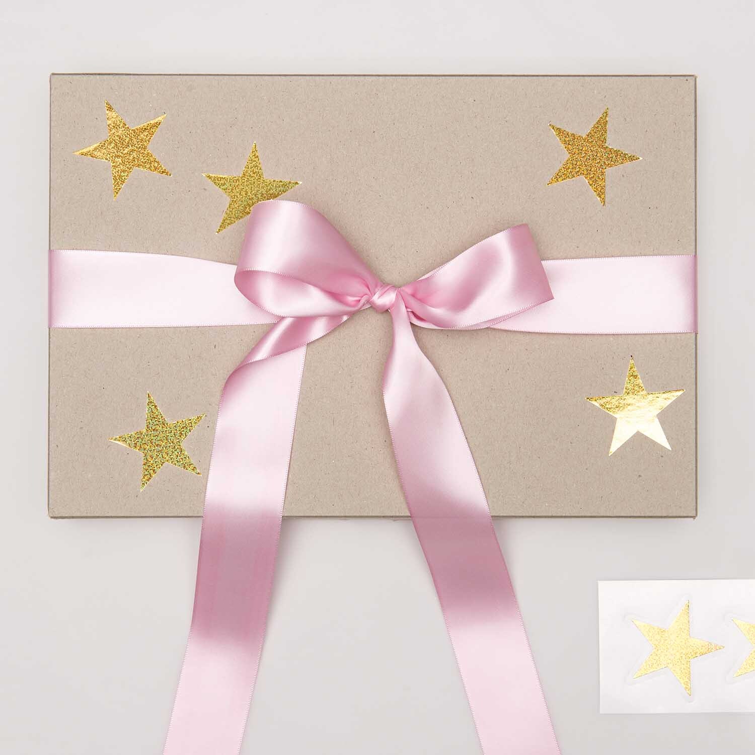 Paper Poetry Sticker Sterne auf Geschenkbox mit rosa Schleife, gold-holographisch glänzend.