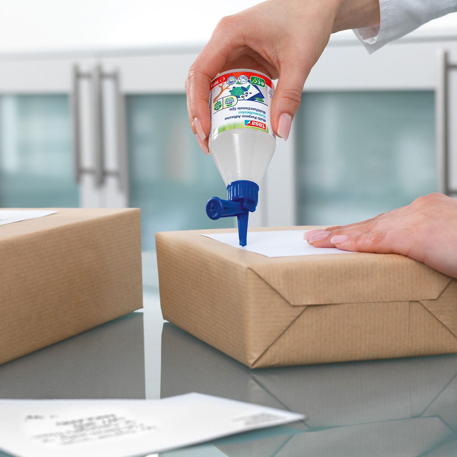 Vielzweckkleber 100g von tesa wird auf ein Paket aufgetragen. Ideal für präzises Kleben.