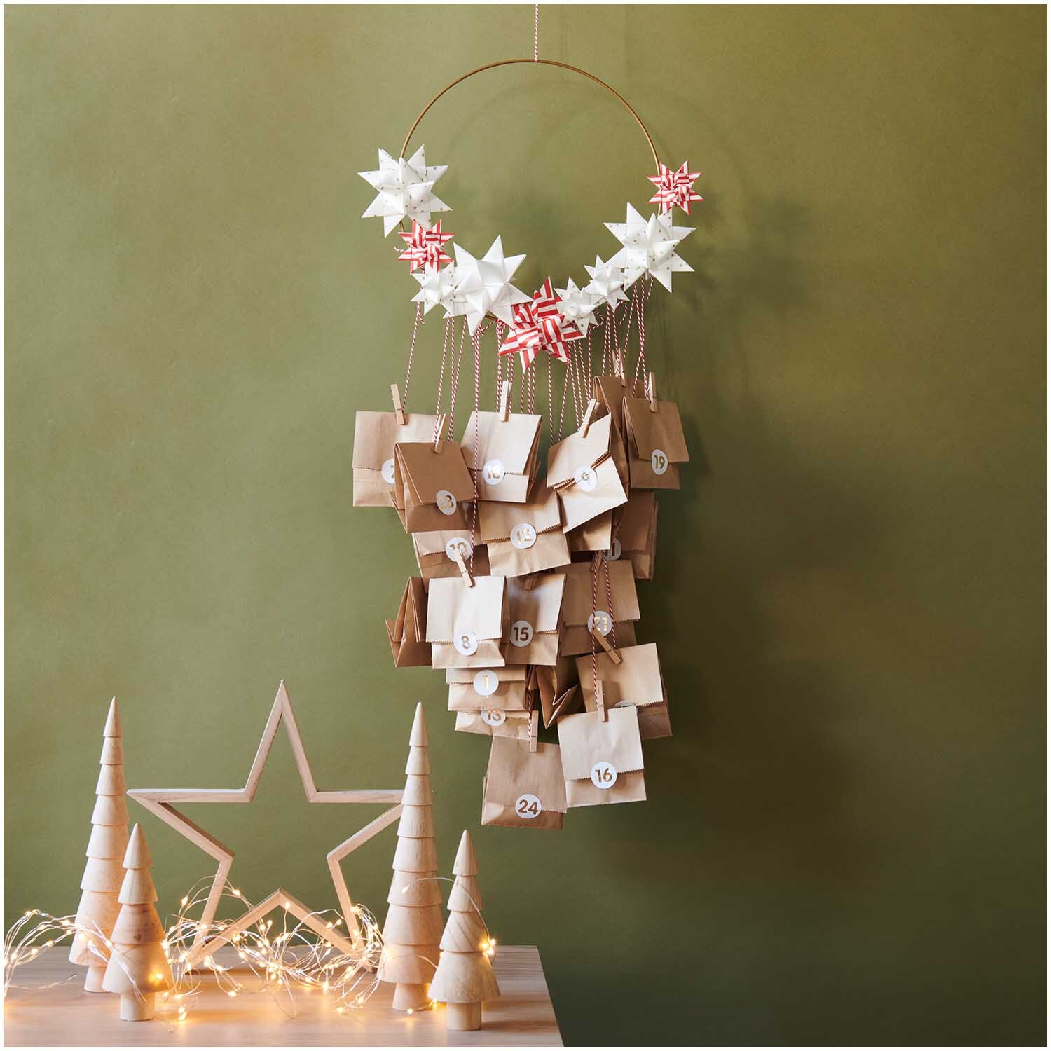 Bastelanleitung Papiertüten-Adventskalender mit Fröbelsternen, dekoriert mit weißen und roten Sternen, vor grünem Hintergrund.