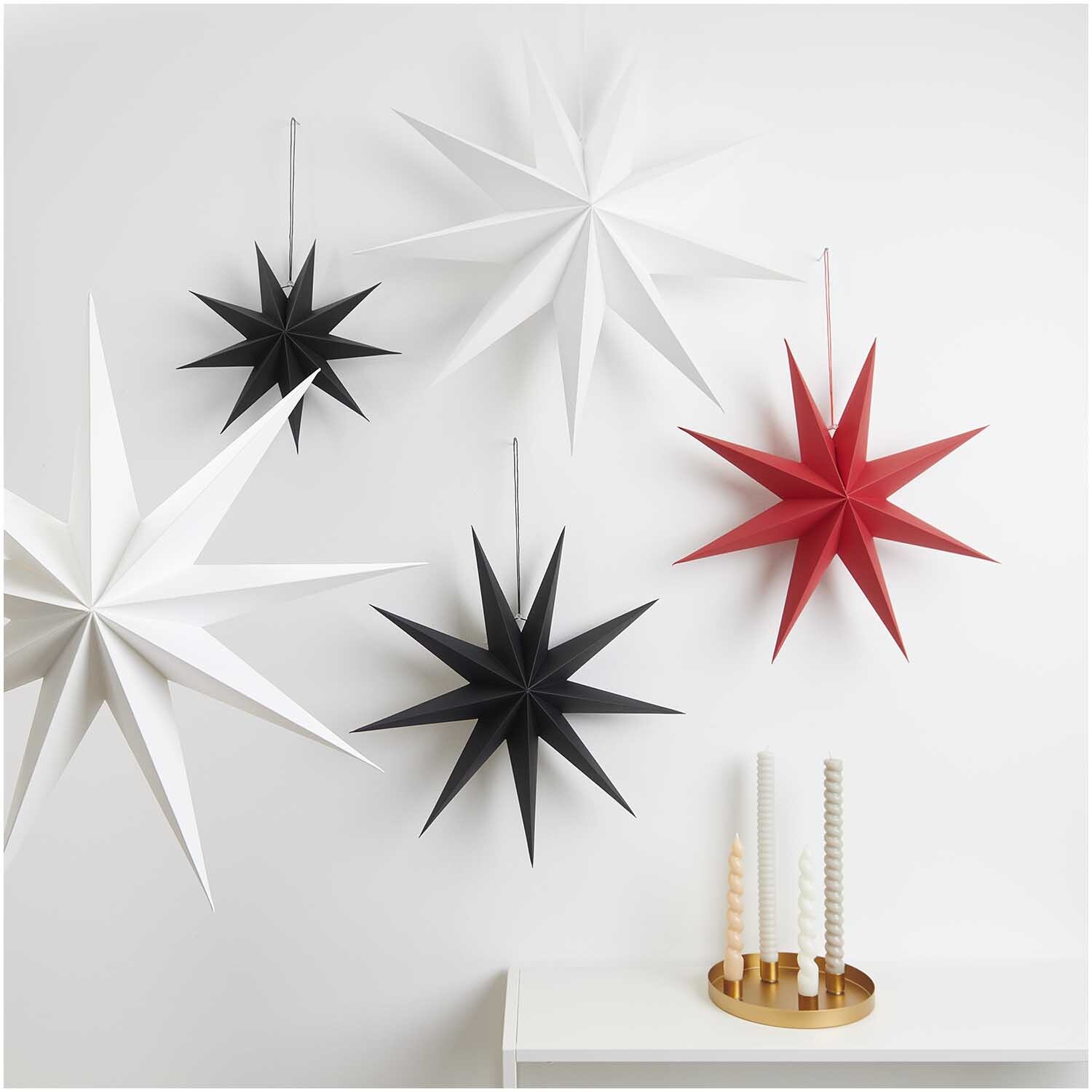 Papierstern auffaltbar 45cm von Rico Design in Rot, dekorativ an der Wand mit anderen Sternen in Schwarz und Weiß arrangiert.