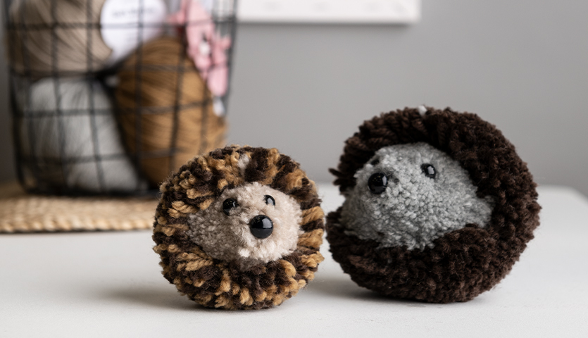 Bastelanleitung Pompon-Igel: Zwei niedliche Pompon-Igel in Braun- und Grautönen auf einem Tisch.