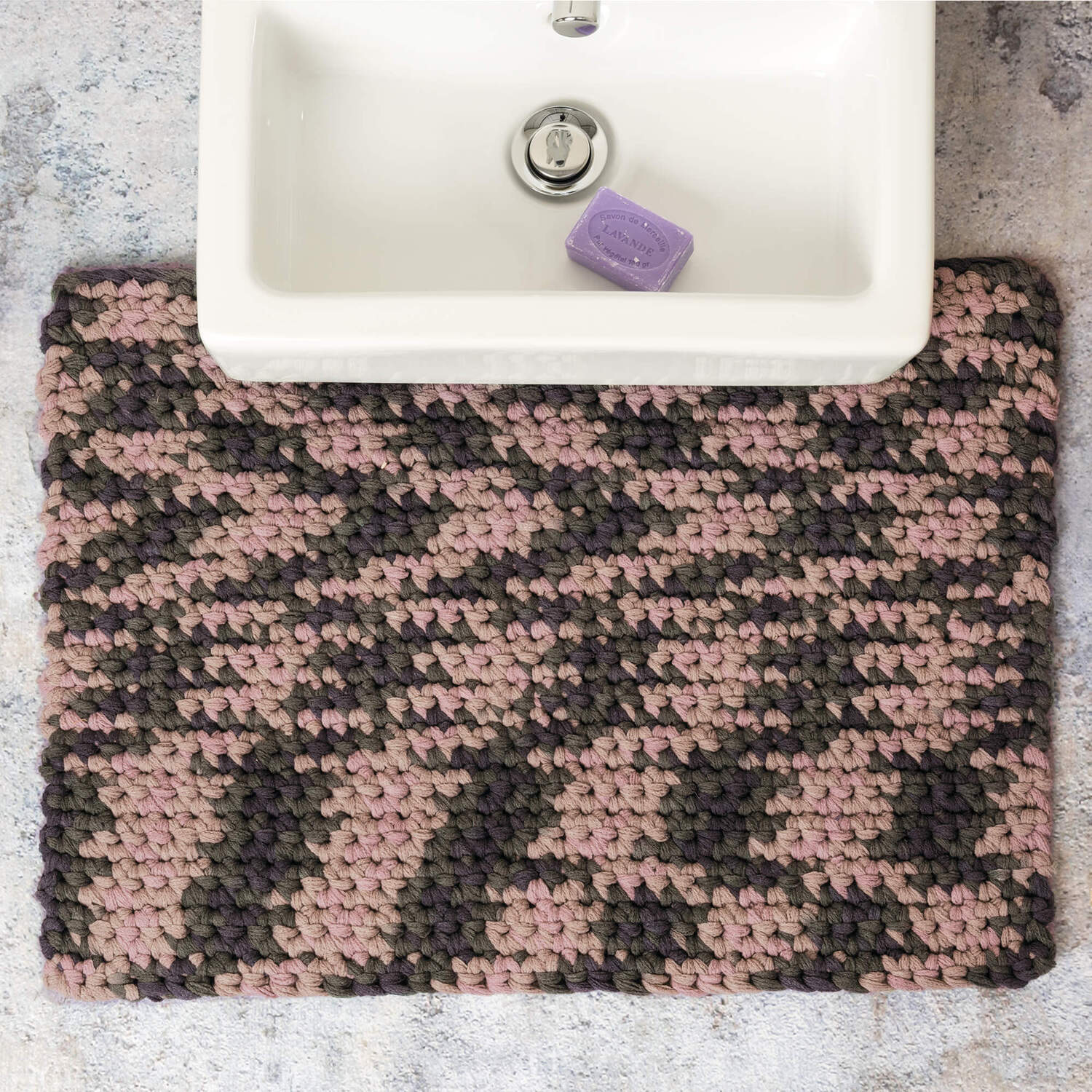 Häkelanleitung Badematte aus Creative Loopy Print: Handgefertigte Matte in Rosa und Grau vor einem Waschbecken mit lila Seife.
